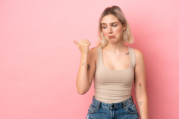 Wall Mural - Young caucasian woman isolated on pink background unhappy and pointing to the side