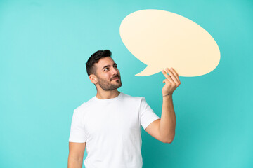 Wall Mural - Young handsome caucasian man isolated on blue background holding an empty speech bubble