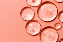 Oil Drops On Salmon Pink Rose Color Background. Clear Liquid Cosmetic Product Macro. Serum Gel Texture With Bubbles Closeup