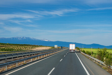 Wall Mural - Refrigerator truck driving along the highway with Sierra Nevada in the background. Rear view.