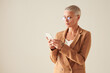© Mediaphotos - Serious blond-haired businesswoman in round glasses standing against white background and using smartphone while reading messages on social medias