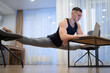Flexible man work on laptop and doing leg-split at home. Concept of originality, creativity and outstanding