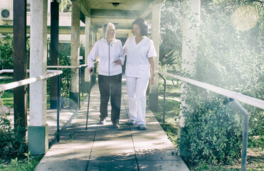 Poster - Asian doctor helping elderly retired woman with walker stick in the hospital yard. Rehabilitation concept