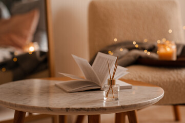 liquid home fragrance in diffuser with open paper book on coffee table in bedroom indoors close up o