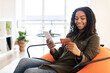 © Prostock-studio - Smiling black lady using phone and credit card at home