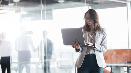 Wall Mural - mature smiling businesswoman at office with group of colleagues on background, working on laptop