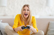 © Prostock-studio - Glad excited pretty young blonde european female in yellow clothes with open mouth plays online games