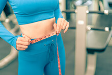 Woman With Slim Body Measuring Her Waistline With Tape In The Fitness Gym.