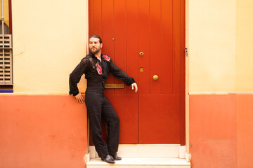 Man dancing flamenco with black shirt and red roses, on the background of a red wooden door, he is waiting leaning on the door. Flamenco dance concept cultural heritage of humanity.