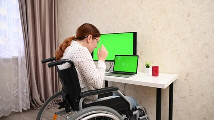 Caucasian woman with disabilities working at the computer while sitting in a wheelchair. 