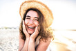 © Davide Angelini - Young joyful woman in white shirt wearing hat smiling at camera on the beach - Traveler girl enjoying freedom outdoors on a sunny day - Wellbeing, healthy lifestyle and happy people concept