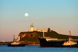 Fototapeta  - Nobbys head lighthouse across Newcastle Harbour with ship and tugboats, Newcastle, NSW, Australia