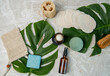 Flatlay nachhaltige biologische Kosmetik mit Braunglasflasche, Tiegel, Creme, Schwamm, Abschminkpads, Bürste, Seife und Q-Tips aus Bambus mit Monstera Blättern im Hintergrund