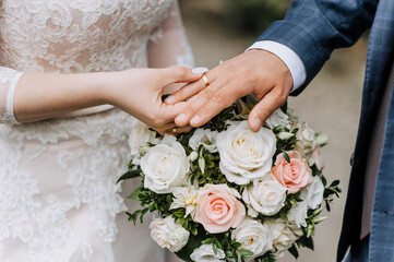 Hands, fingers with gold rings of the bride and groom close-up at the wedding ceremony against the background of a bouquet. Wedding photography, portrait, concept.