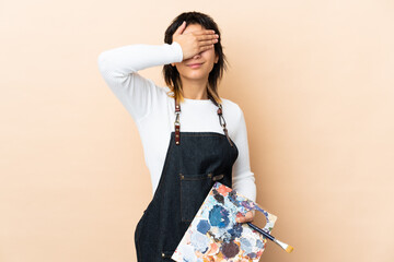 Wall Mural - Young artist man holding a palette over isolated background covering eyes by hands