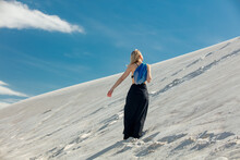 Woman With Blue Net Bag Walking On White Sand Dune In Desert In Summer