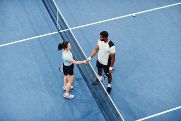 Minimal top view of two tennis players shaking hands across net during match, copy space