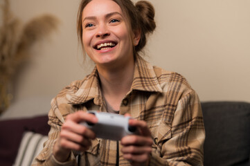 Wall Mural - A young pretty girl plays a video game on a beige background. Close-up. The girl laughs, rejoices to win. Online games with friends, entertainment, win, prizes, surprises, virtual reality.