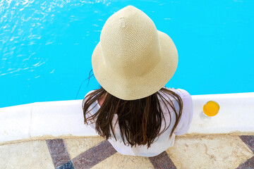 Wall Mural - Back view young adult female woman person enjoy relaxing on swimming pool edge in luxury hotel resort outdoor looking on blue clear water. Summer travel tropical recreational vacation tourism concept