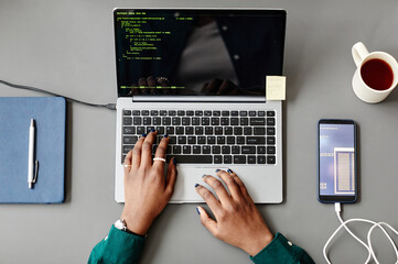 Minimal top view of unrecognizable black woman using laptop and writing code at grey workplace desk