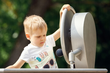 Outdoor portrait of happy little boy playing inside of city fountain on a hot summer day