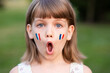 © Svetlana - Portrait of surprised 7 years old child with painted cheeks in flag of France walking outdoor. Cute little girl screaming with opened mouth and crazy expression looking at camera.