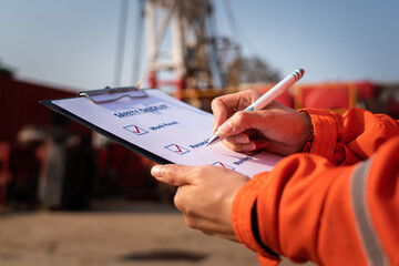 Wall Mural - Construction worker is using a pen to checking on checklist - Safety audit and inspection working action with blurred background of machinery. Selective focus at hand.