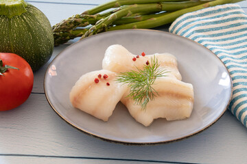 Wall Mural - raw halibut fillet in a plate with fresh vegetables on a table