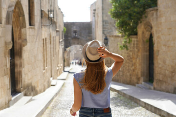 Wall Mural - Tourism in Rhodes, Greece. Back view of traveler girl goes down the Street of the Knights of Rhodes city, Greece. Young female traveler visiting southern Europe.