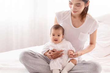 Asian mother holding infant and looking baby with love and tender, mom play with toddler. Beautiful Asian women in white casual t-shirt and newborn in white cotton soft textile.