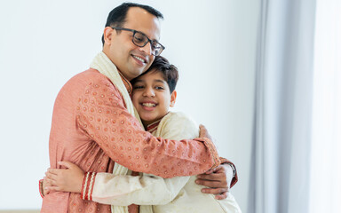 Portrait two people of happy single Indian father, teenage handsome son hugging with warmth, love, wearing traditional clothes, smiling in cozy indoor home. Family, Education, Lifestyle Concept.