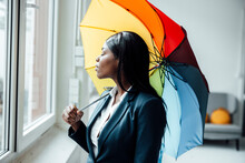 Businesswoman With Eyes Closed Holding Colorful Umbrella In Office