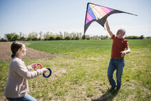 Grandfather Teaching Granddaughter Flying Kite On Field
