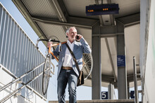 Smiling Businessman Carrying Bicycle On Shoulder Talking Through Smart Phone At Railroad Station