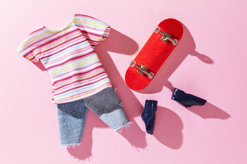 Small fingerboard and toy clothes on a pink background, top view