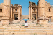 Young tourist standing with hat and open arms  in old city of Jerash, ancient building in Jordan