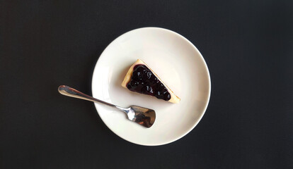 Wall Mural - Top view of slice of blueberry cheesecake and stainless steel spoon in white dish or plate on black background with copy space. Flat lay of sweet dessert and Homemade food on dark table