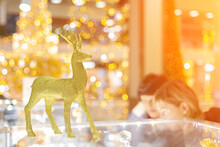 A Golden Shiny Christmas Deer Stands On A Glass Shop Counter Against A Background Of Bright Bokeh