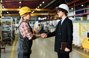 Two engineers of large modern factory shaking hands after discussion of terms of new project and making agreement in factory