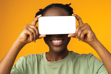 Young smiling african american woman showing smartphone with blank screen against yellow background