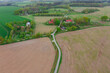 Droga polna przebiegająca przez pola i łąki widziana z wysokości. Zdjęcie z drona. W oddali widać zabudowania pobliskiej wioski.