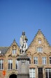Statue von Hans Memling am Woensdagmarkt mit schönen alten Treppengiebeln aus Backstein vor blauem Himmel im Sonnenschein in den Gassen der Altstadt von Brügge in Westflandern in Belgien