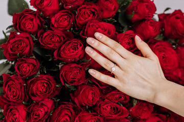 Wall Mural - she said yes. close-up of woman hand with engagement rings. Hand of the on the background of the big bouquet of red roses. romantic proposal time