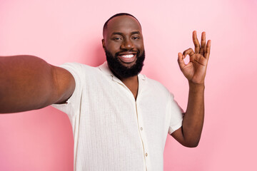 Wall Mural - Portrait of positive funky man make selfie hand fingers demonstrate okey isolated on pink color background