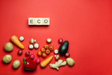 Wall Mural - Top view of organic vegetables near eco lettering on cubes on red background.