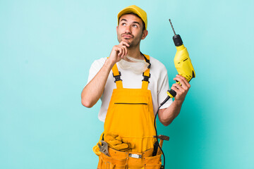 young adult hispanic man thinking, feeling doubtful and confused. worker and drill concept