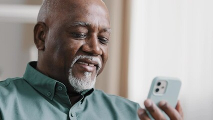 Mature elderly old African 60s biracial man using phone American businessman male grandfather free wi-fi chatting mobile app at home browsing net texting message in smartphone internet technology