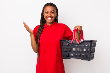 Wall Mural - young adult black woman feeling happy, surprised realizing a solution or idea. empty shopping basket concept