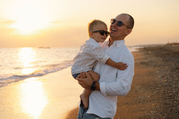 Wall Mural - Happy Father's day. Father and baby play on the beach. Dad and him Child together enjoying sunset. Loving single father hugs cute little son.