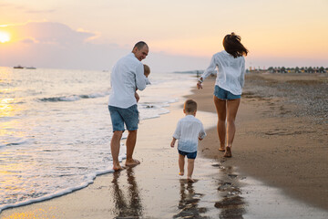 Wall Mural - Happy family having fun playing beach in summer vacation on the beach. Happy family and vacations concept. Seascape at sunset with beautiful sky. Family on the beach.